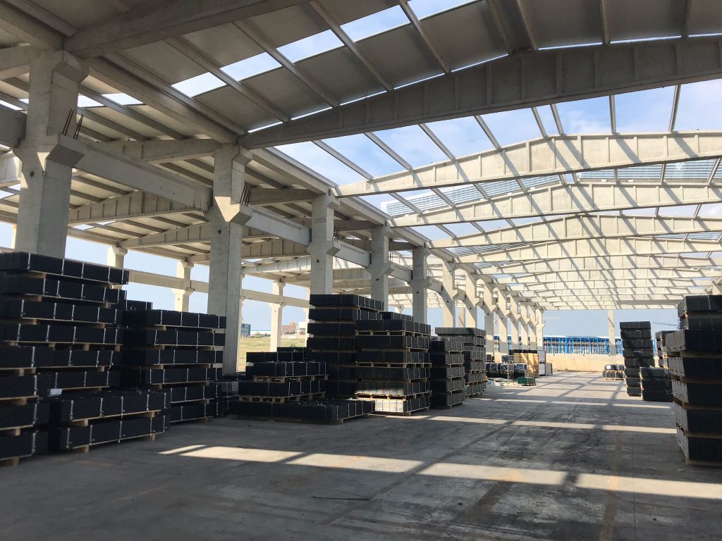 Prefabrik betonarme çatılı üretim holünün içi; zeminde istiflenmiş kutu profil demetleri